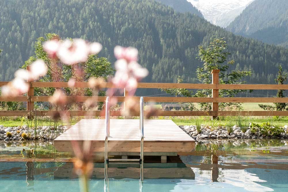 Passerelle en bois d'une biopiscine avec des fleurs et vue sur les montagnes