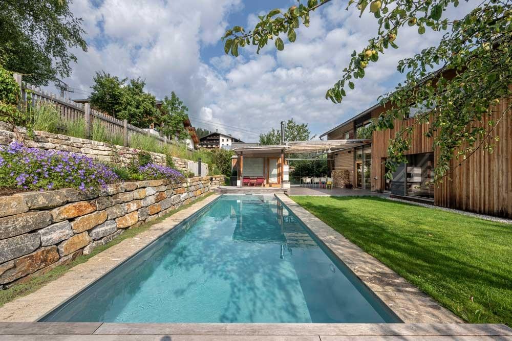 Biopool moderne dans le jardin avec maison en bois et mur en pierre naturelle