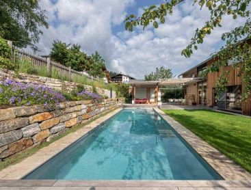 Biopool moderne dans le jardin avec maison en bois et mur en pierre naturelle