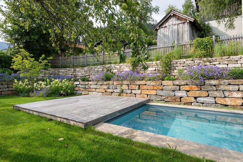 Biopool avec terrasse en bois, mur en pierre naturelle et fleurs