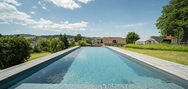 Living Pool avec une surface d'eau claire et une bordure en bois dans un jardin avec vue sur le paysage