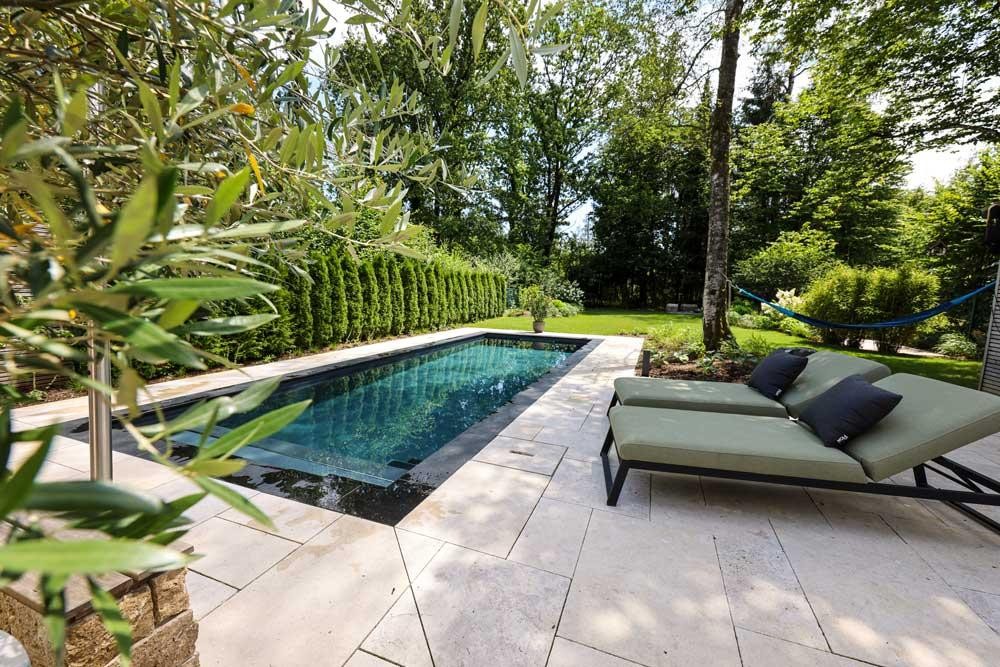 Piscine naturelle design avec terrasse en pierre claire et bains de soleil dans un jardin calme