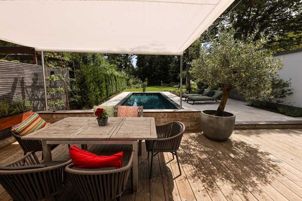 Piscine naturelle design avec terrasse en bois voile d’ombrage et coin repas au jardin
