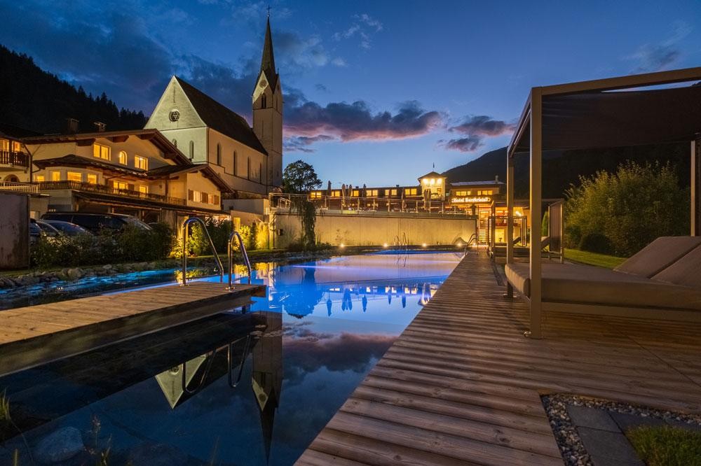 Piscine d’hôtel avec terrasse en bois au crépuscule à côté d’une église