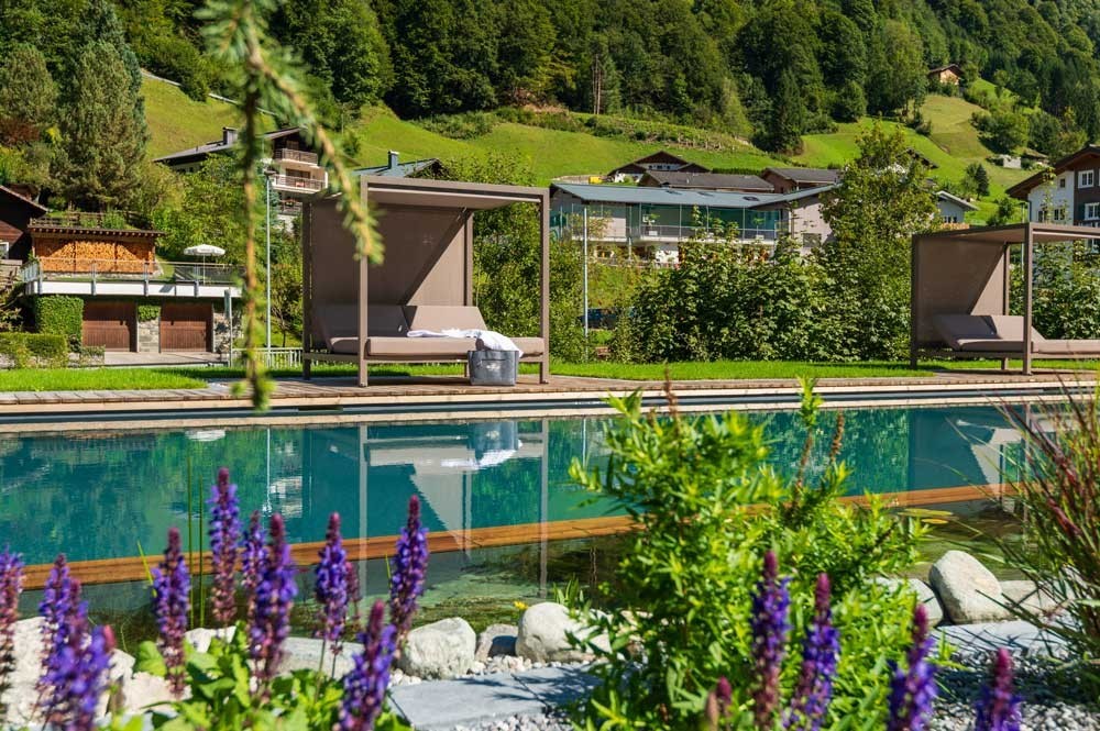 Piscine d’hôtel avec lits de repos et panorama alpin dans un cadre verdoyant