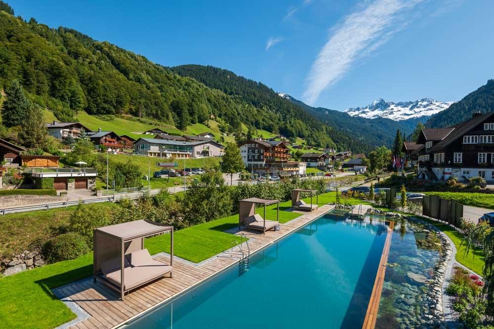 Vue aérienne d’une piscine d’hôtel dans un village alpin avec décor montagneux