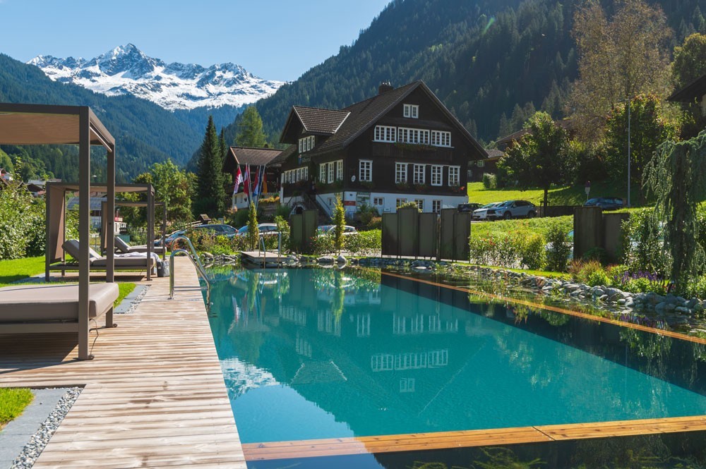 Piscine d’hôtel avec vue sur la montagne devant un hôtel alpin et terrasse bois
