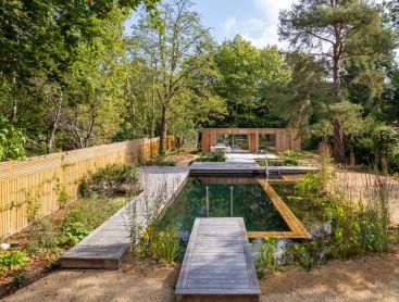Piscine naturelle avec terrasse en bois dans un grand jardin urbain devant une maison en briques