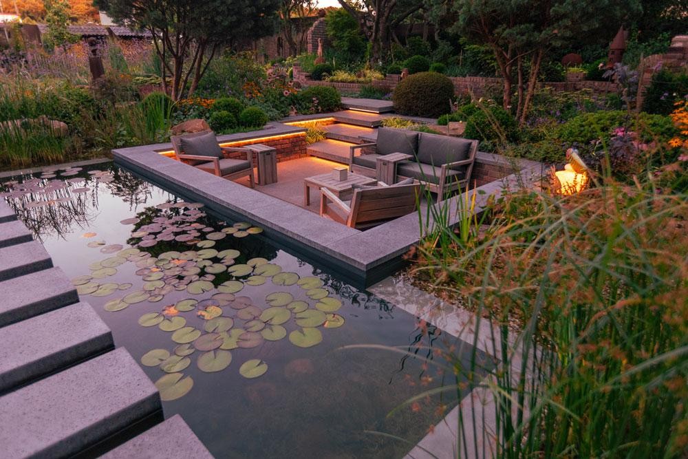 Salon au bord de la piscine naturelle avec nenuphars et lumiere du soir
