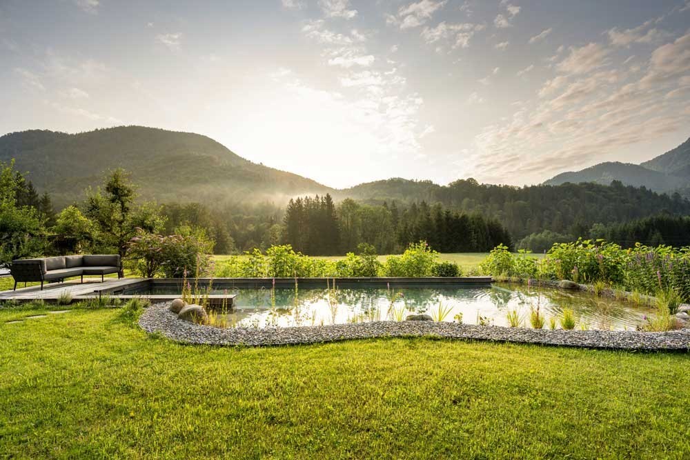 Piscine naturelle dans un jardin idyllique au lever du soleil entourée de montagnes