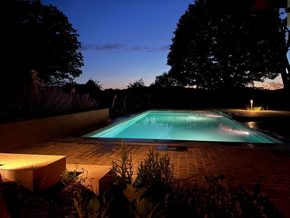 Piscine naturelle éclairée le soir dans une ambiance de jardin