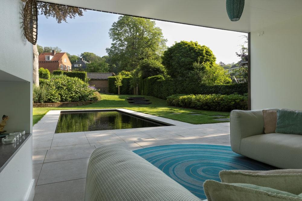 Vue depuis le salon sur la piscine naturelle, la terrasse et le jardin